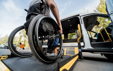Osoba na wózku inwalidzkim wjeżdża na podjazd przystosowanego busa.