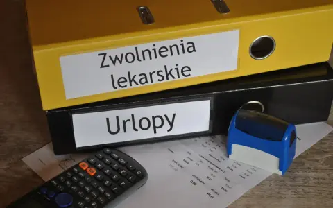 Dwa segregatory z napisami "Zwolnienia lekarskie" i "Urlopy", kalkulator, pieczątka i dokumenty.