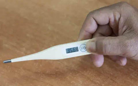 Dłoń trzyma termometr, który pokazuje 35.6°C. To niska temperatura, która może być objawem problemów zdrowotnych, np. podczas choroby covid.
