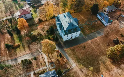 Widok z lotu ptaka na wieś z budynkami i jesiennymi drzewami pokrytymi liśćmi.