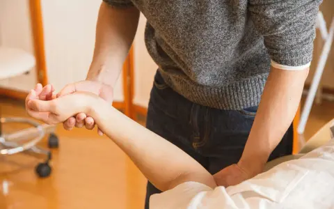 Fizjoterapeuta masuje przedramię pacjenta.