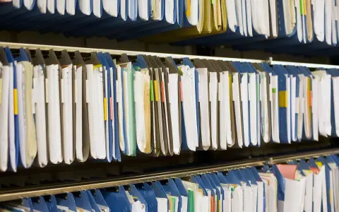 Rzędy wiszących segregatorów, gotowych do archiwizacji dokumentów. Widać tu wiele teczek, niektóre z kolorowymi etykietami, idealne do organizacji pracy, np. z wykorzystaniem systemu druk erp-6.