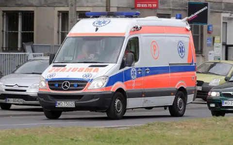 Karetka na sygnale z oznaczeniami medycznymi, jadąca ulicą.