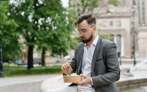 Mężczyzna w garniturze je sałatkę na zewnątrz.