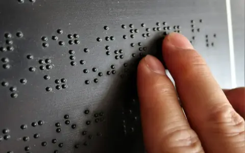 Dłoń czytająca tekst Braille'a na czarnej powierzchni.