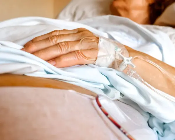 Dłoń pacjenta z wenflonem, przygotowująca się do podróży ze szpitala do hospicjum.