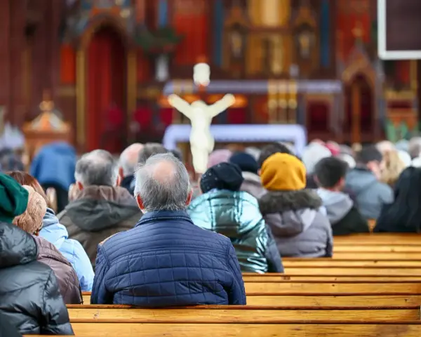 Ludzie siedzący w kościele, widok od tyłu, w tle ołtarz z krzyżem.