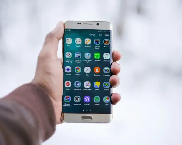 Dłoń trzymająca złoty telefon Samsung z ikonami aplikacji na ekranie.
