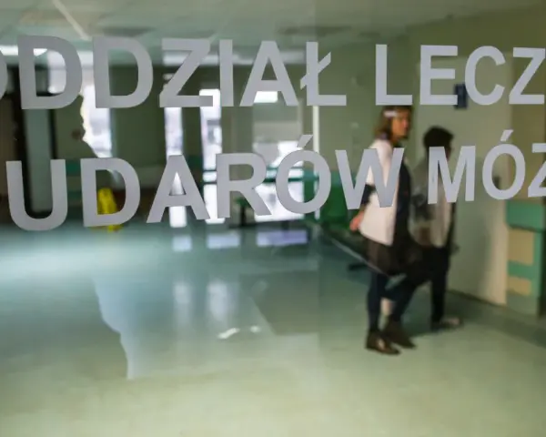Drzwi do oddziału leczenia udarów mózgu. W środku widać personel medyczny i pacjentów, gotowych na zabiegi takie jak trombektomia.