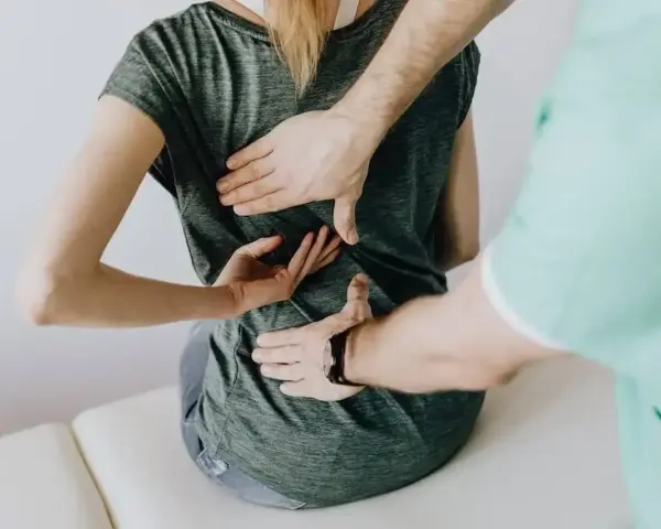 Fizjoterapeuta bada plecy pacjentki. Lekarz lub fizjoterapeuta wystawia zwolnienie na czas rehabilitacji.