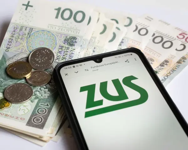 Telefon z logo ZUS na tle polskich banknotów i monet.