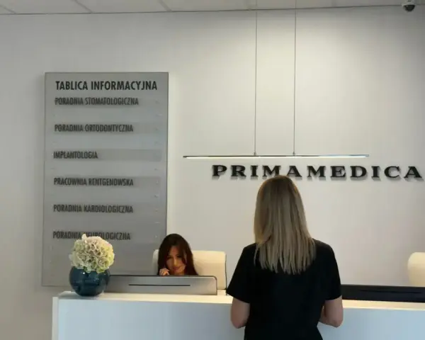 Recepcja gabinetu stomatologicznego Primamedica z tablicą informacyjną i pracownicą.