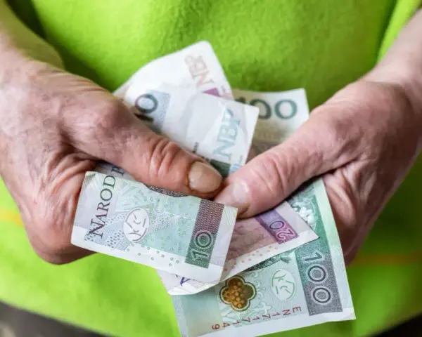 Dłonie trzymające polskie banknoty: 10, 20 i 100 złotych.