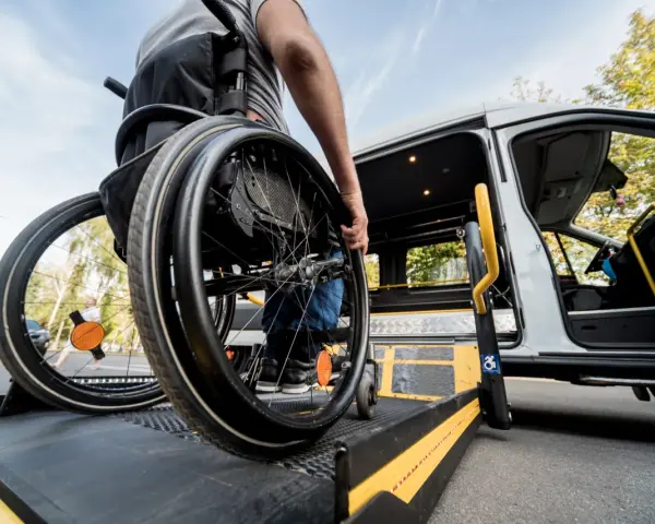 Osoba na wózku inwalidzkim wjeżdża na podjazd przystosowanego busa.