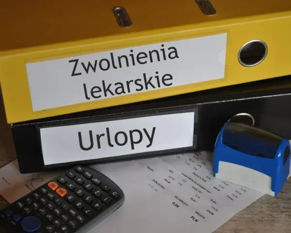 Dwa segregatory z napisami "Zwolnienia lekarskie" i "Urlopy", kalkulator, pieczątka i dokumenty.