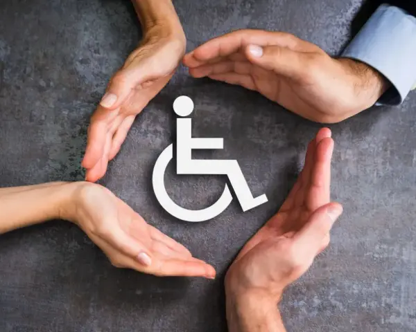 Symbol wózka inwalidzkiego otoczony dłońmi symbolizującymi wsparcie i opiekę.