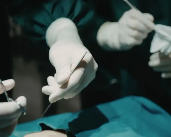 Dłonie chirurga w rękawiczkach trzymające narzędzia chirurgiczne i gazę podczas operacji.