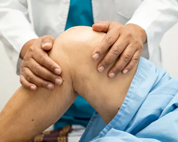 Fizjoterapeuta delikatnie masuje kolano pacjenta w niebieskiej koszuli.