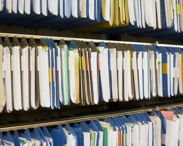 Rzędy wiszących segregatorów, gotowych do archiwizacji dokumentów. Widać tu wiele teczek, niektóre z kolorowymi etykietami, idealne do organizacji pracy, np. z wykorzystaniem systemu druk erp-6.