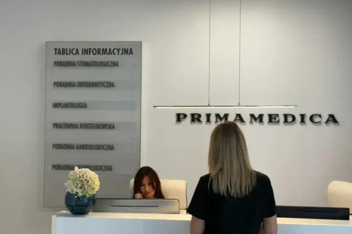 Recepcja gabinetu stomatologicznego Primamedica z tablicą informacyjną i pracownicą.