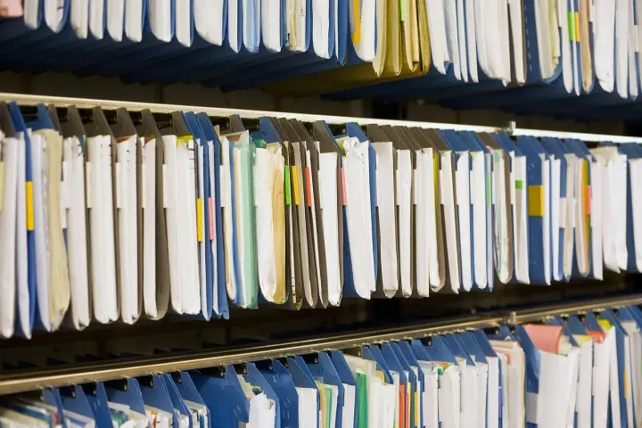 Rzędy wiszących segregatorów, gotowych do archiwizacji dokumentów. Widać tu wiele teczek, niektóre z kolorowymi etykietami, idealne do organizacji pracy, np. z wykorzystaniem systemu druk erp-6.