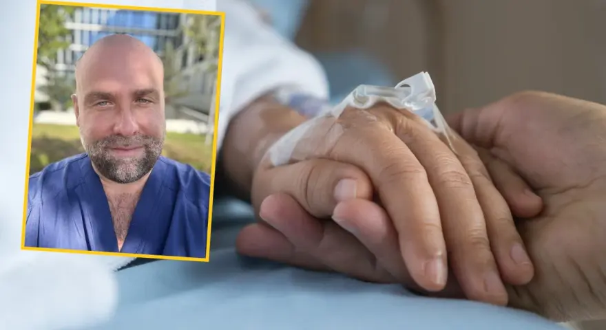 Uśmiechnięty mężczyzna w niebieskim uniformie medycznym podaje słowa otuchy choremu na raka, trzymając go za rękę z wenflonem.