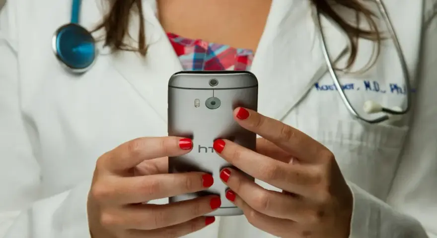 Lekarz w białym kitlu trzyma smartfon, na którym widać aparat i logo HTC.