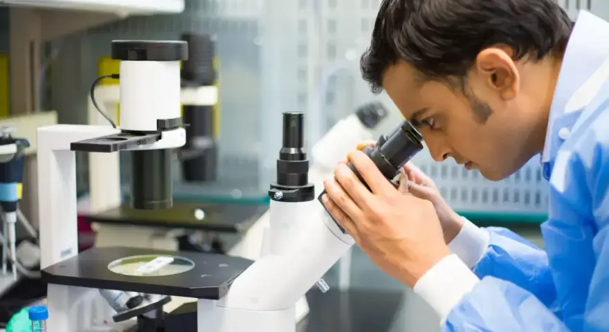 Mężczyzna w niebieskiej fartuchu laboratoryjnym bada próbkę pod mikroskopem, kluczowy element w diagnostyce patomorfologia.