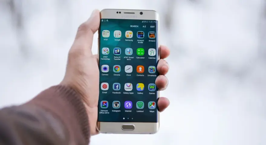 Dłoń trzymająca złoty telefon Samsung z ikonami aplikacji na ekranie.