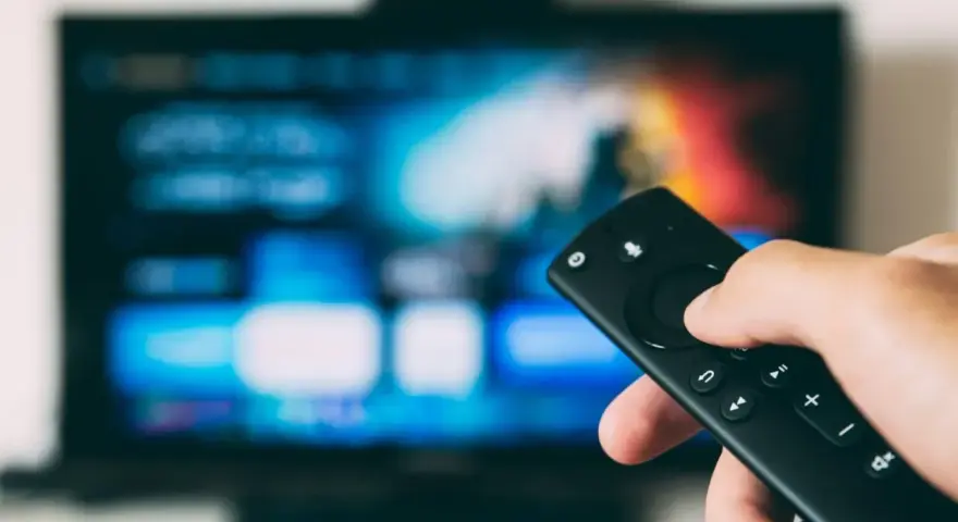 Dłoń trzyma pilota, celując w ekran telewizora. Szukasz sposobu, jak wyłączyć lektora dla niewidomych?