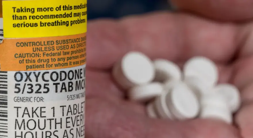 Butelka z lekiem Oxycodone i garść tabletek w dłoni.