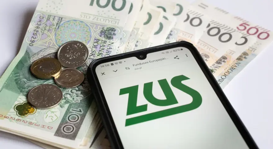 Telefon z logo ZUS na tle polskich banknotów i monet.