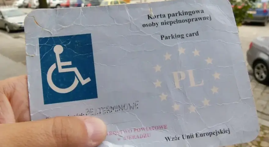 Karta parkingowa dla niepełnosprawnych, z symbolem wózka inwalidzkiego i oznaczeniem PL. Ułatwia parkowanie w mieście.