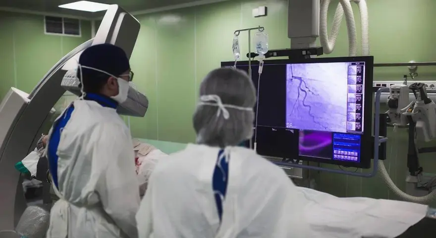 Lekarze w sterylnym stroju analizują obraz z koronarografii na monitorze w sali operacyjnej.