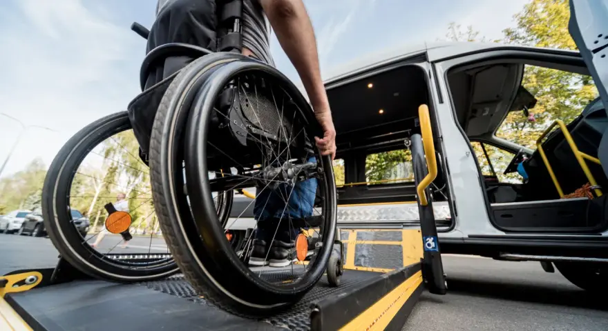 Osoba na wózku inwalidzkim wjeżdża na podjazd przystosowanego busa.
