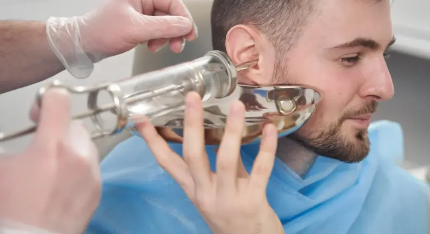 Lekarz w rękawiczce wykonuje płukanie ucha pacjentowi za pomocą strzykawki.