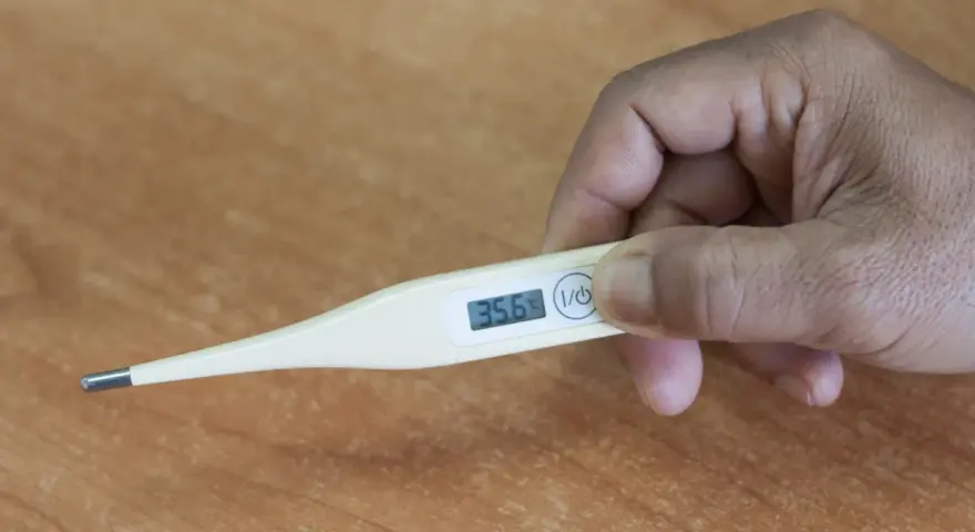 Dłoń trzyma termometr, który pokazuje 35.6°C. To niska temperatura, która może być objawem problemów zdrowotnych, np. podczas choroby covid.