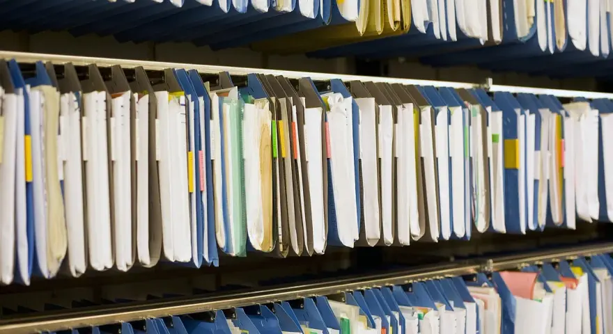 Rzędy wiszących segregatorów, gotowych do archiwizacji dokumentów. Widać tu wiele teczek, niektóre z kolorowymi etykietami, idealne do organizacji pracy, np. z wykorzystaniem systemu druk erp-6.