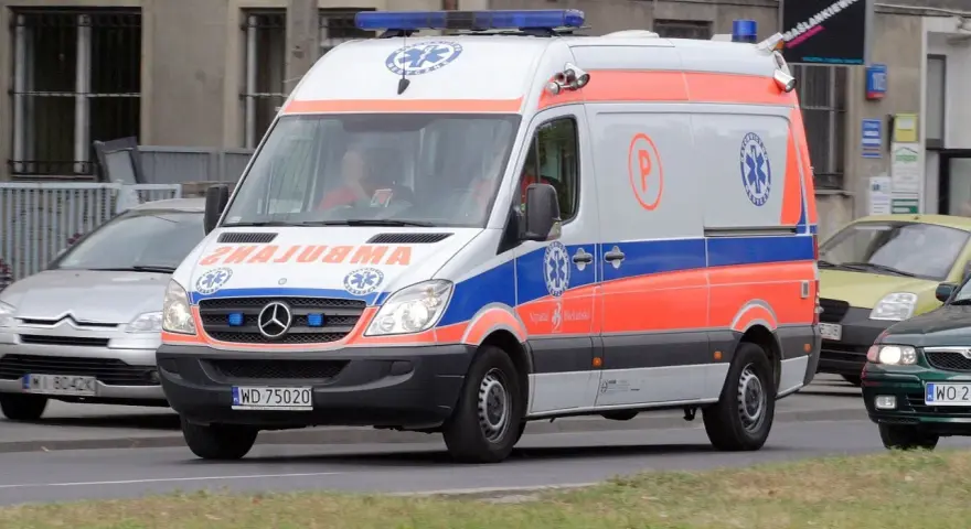 Karetka na sygnale z oznaczeniami medycznymi, jadąca ulicą.