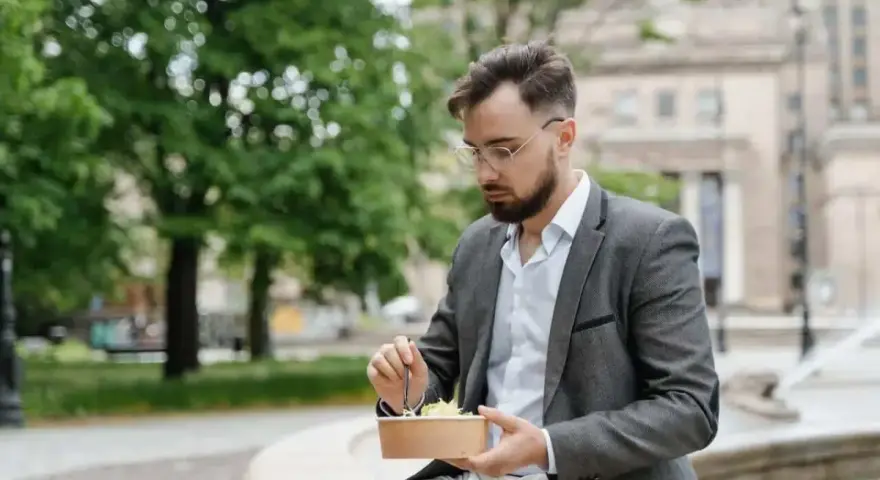 Mężczyzna w garniturze je sałatkę na zewnątrz.