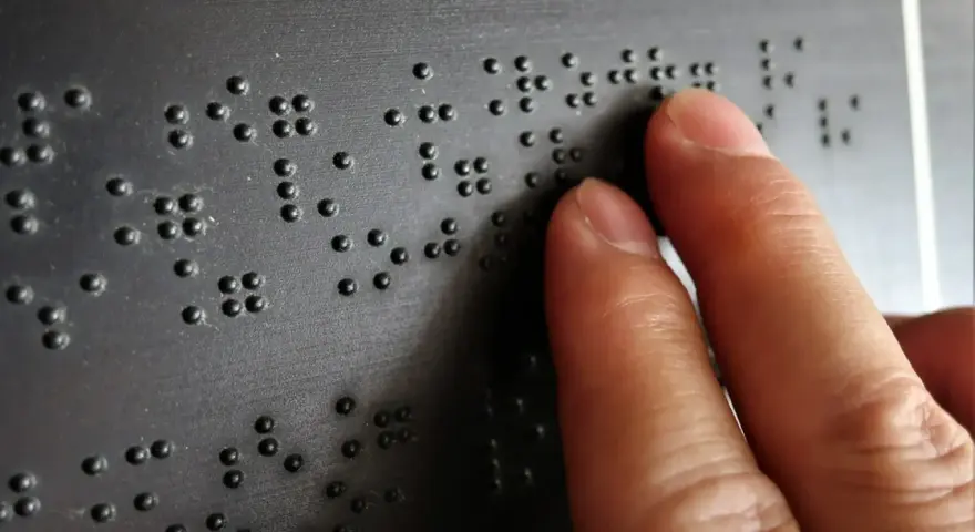 Dłoń czytająca tekst Braille'a na czarnej powierzchni.