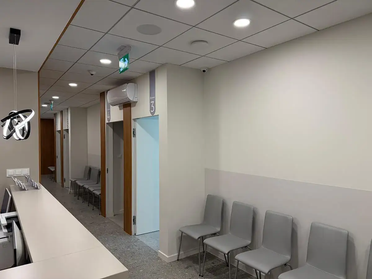 Nowoczesna poczekalnia z rzędem szarych krzeseł, ladą recepcyjną i drzwiami gabinetów.