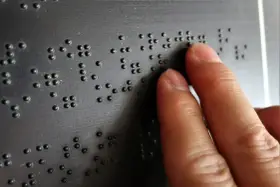 Dłoń czytająca tekst Braille'a na czarnej powierzchni.