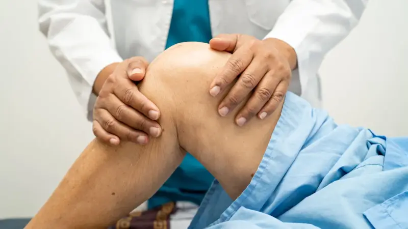 Fizjoterapeuta delikatnie masuje kolano pacjenta w niebieskiej koszuli.